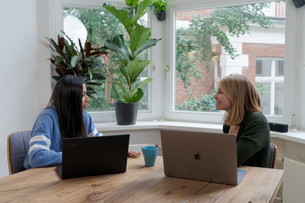 Two women collaborate at a table with laptops, discussing a strategy for account planning.